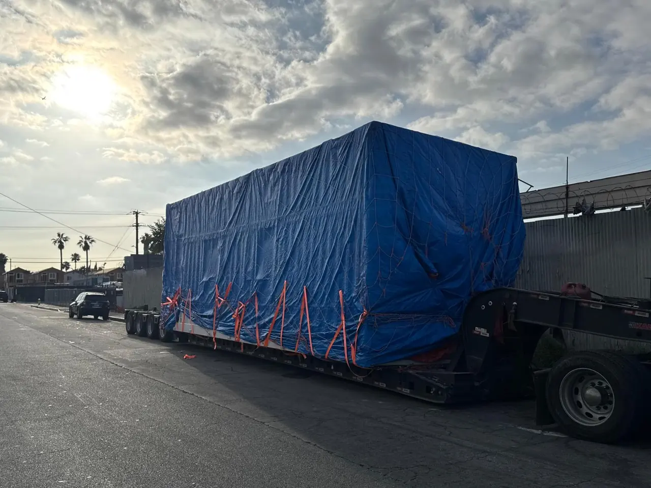 Large blue-tarped load secured with straps on a lowboy trailer