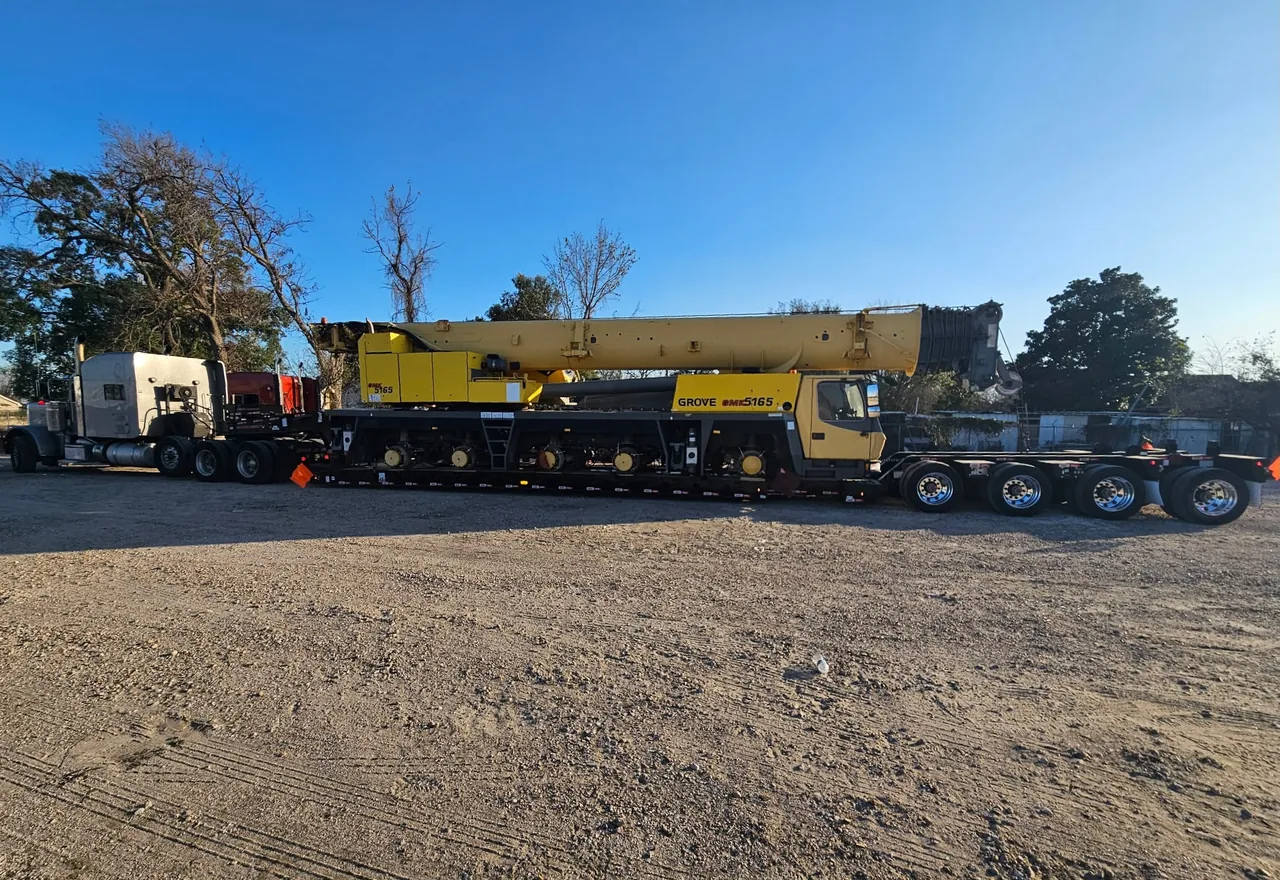 Yellow Grove mobile crane secured on a long lowboy trailer behind a truck