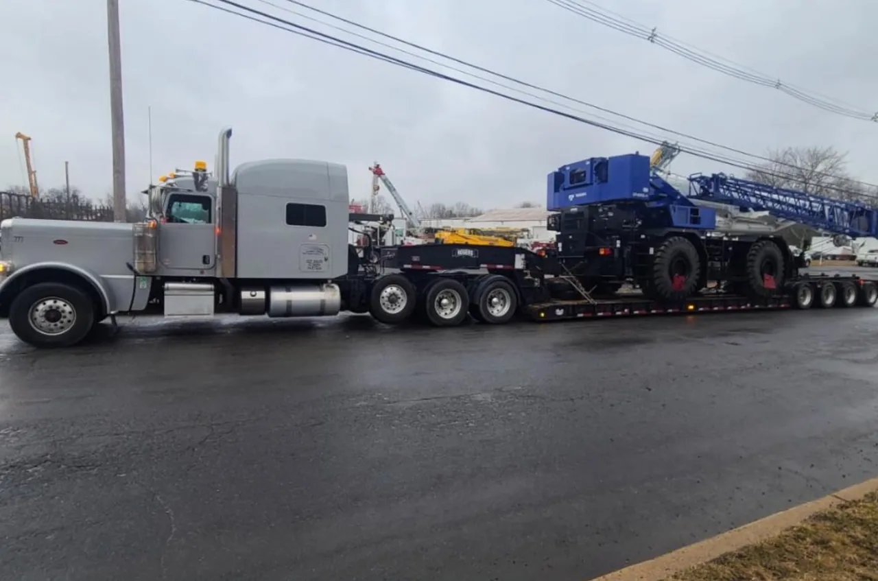Silver truck hauling a blue mobile crane on a lowboy trailer