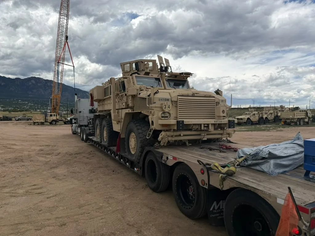 Front view of a tan military vehicle loaded on a trailer at a loading site