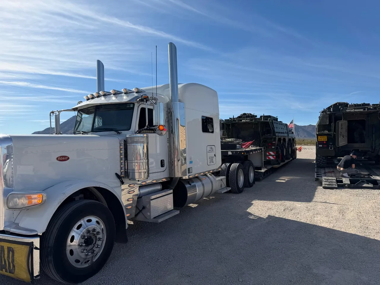 Silver Green Way truck and trailer carrying military equipment at a staging area